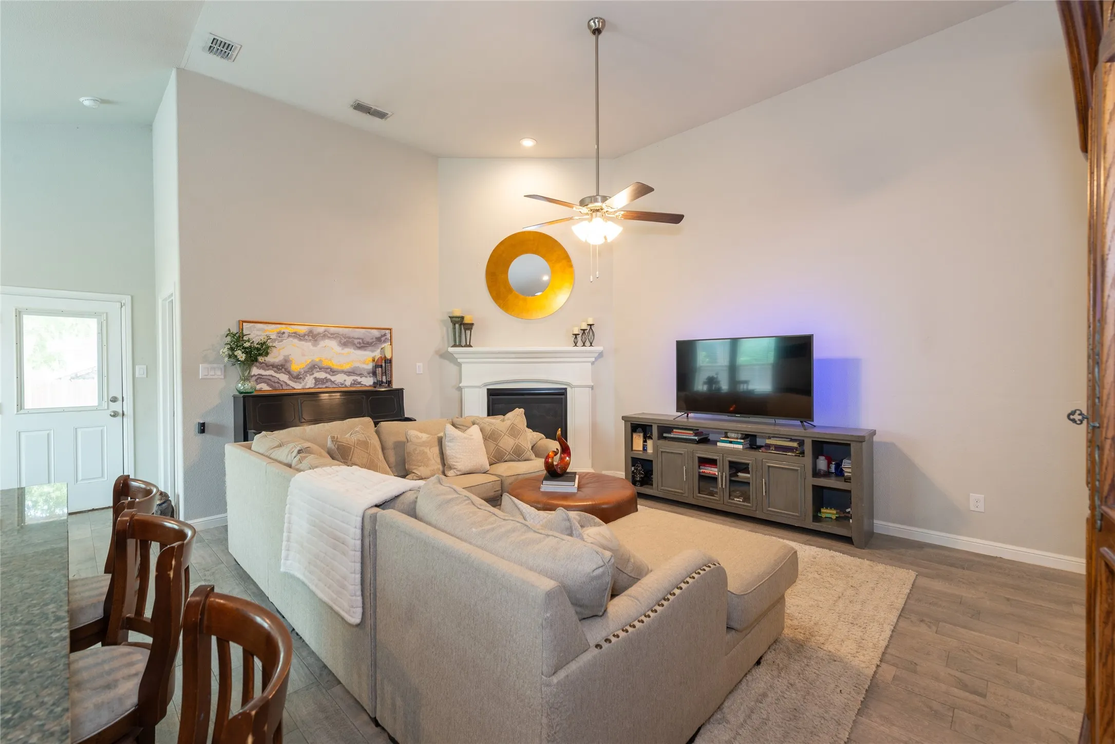 Vaulted ceilings, a built-in fireplace, wood-finish flooring, and a ceiling fan with integrated lighting