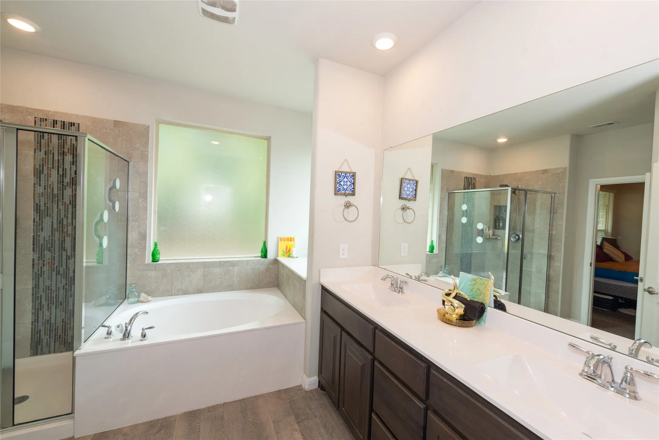 Spacious bathroom featuring a corner soaking tub, separate glass-enclosed shower with tile surround, dual vanity with undermount sinks, wood-finish cabinetry, and wide mirror