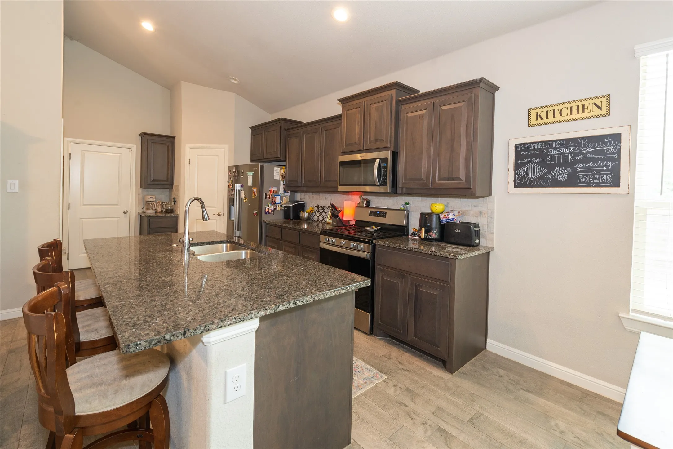 Kitchen featuring wood-finish flooring, vaulted ceilings, a large island with an undermount sink, and dark wood cabinetry