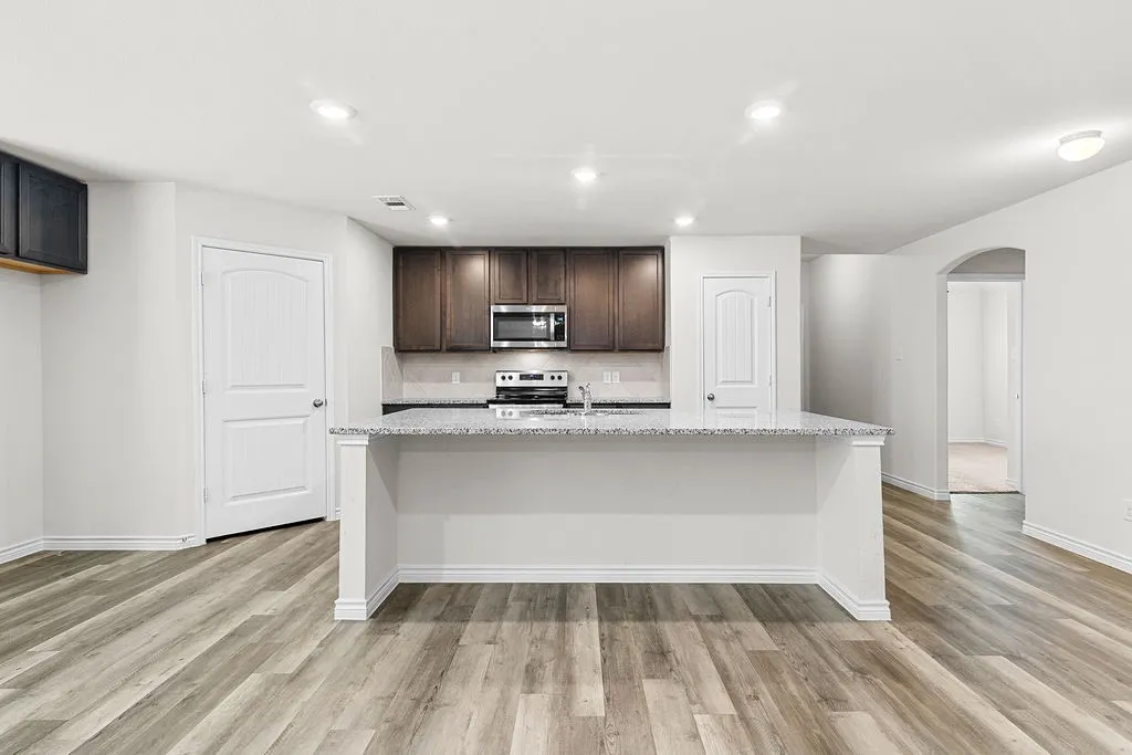 Open-concept kitchen with wood-finish flooring, dark wood cabinetry, and light-toned countertops