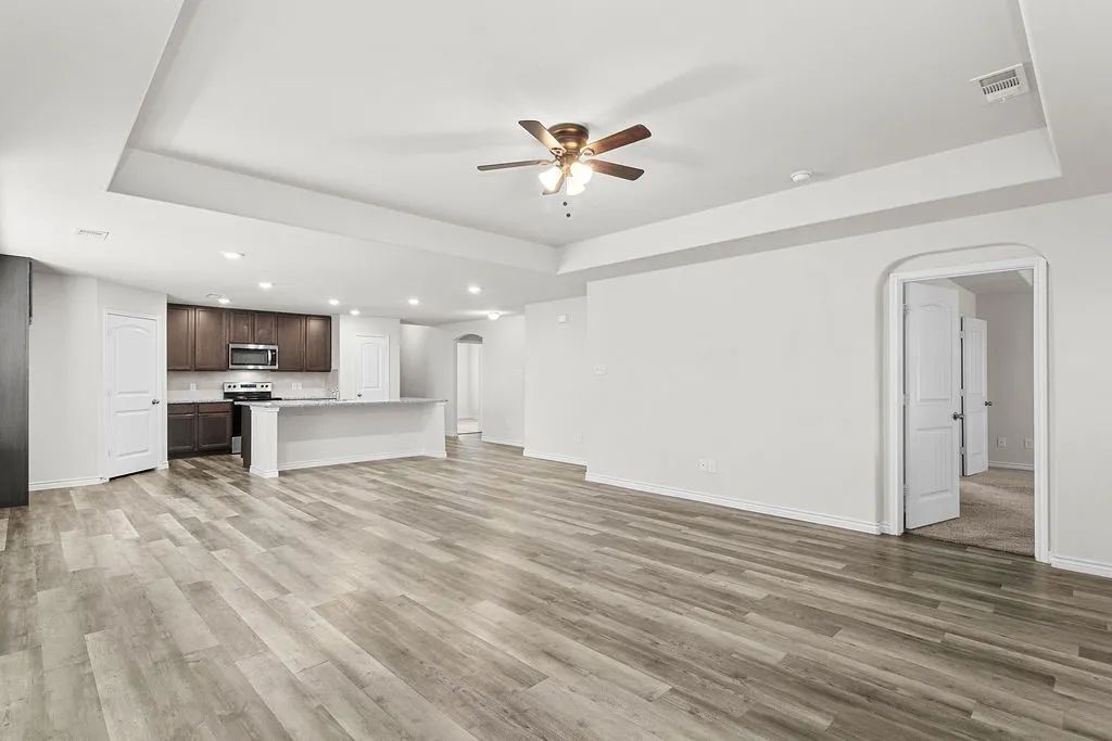 Spacious open-concept interior featuring light wood-finish flooring, a tray ceiling with a ceiling fan, and recessed lighting