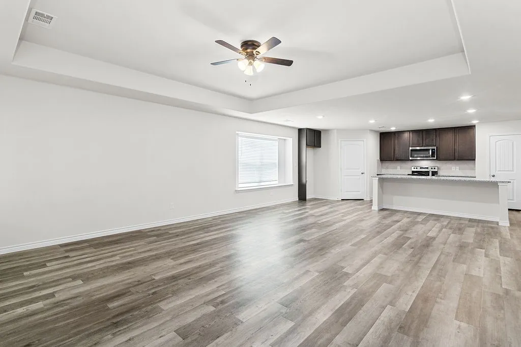 Open-concept living space featuring wood-finish flooring, a tray ceiling, and a ceiling fan