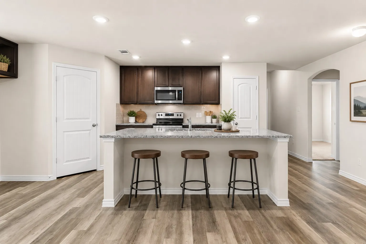 Kitchen featuring wood-finish flooring, recessed lighting, dark wood cabinetry, a granite-finish island with an integrated sink, and stainless steel appliances