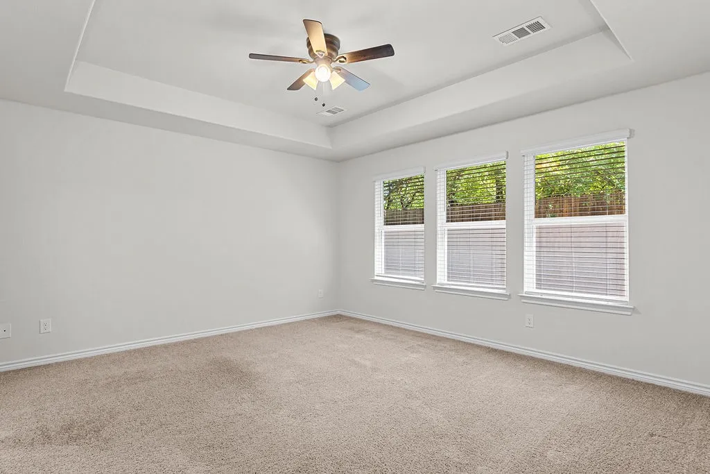 Tray ceiling with a ceiling fan, three windows with blinds, and neutral carpeting