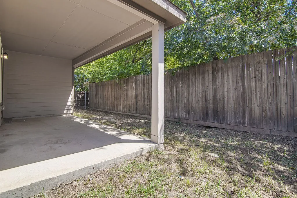 Covered concrete patio with an attached exterior light fixture and a wood privacy fence
