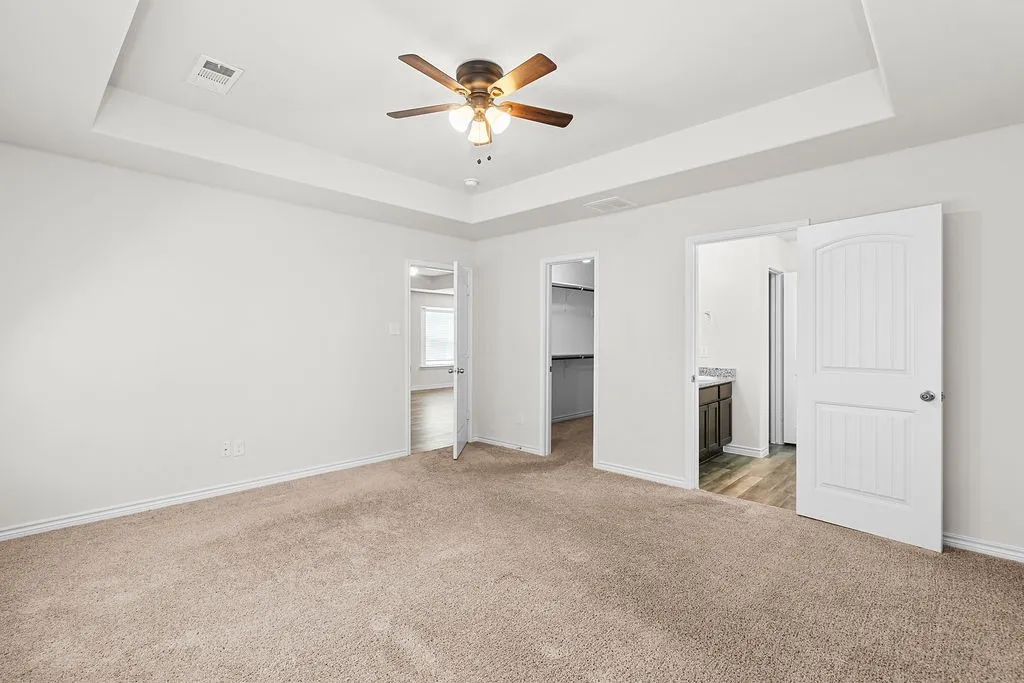 Tray ceiling with a ceiling fan, carpet flooring, panel doors, and a vanity with a countertop