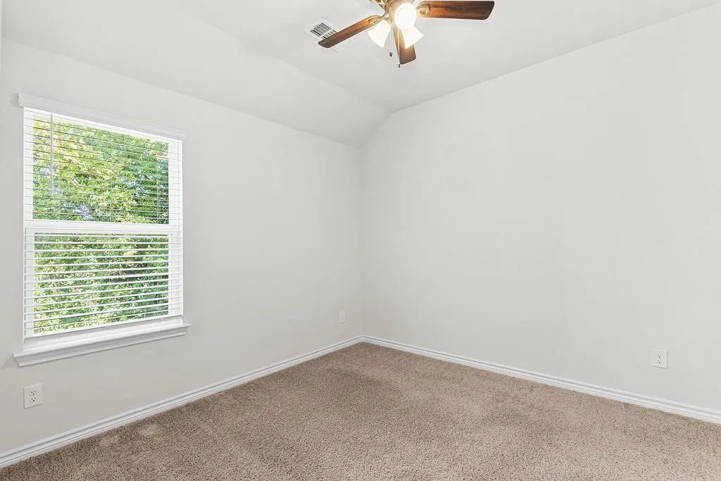 Neutral wall paint with textured carpet flooring, a window with blinds, and a ceiling fan with integrated lighting