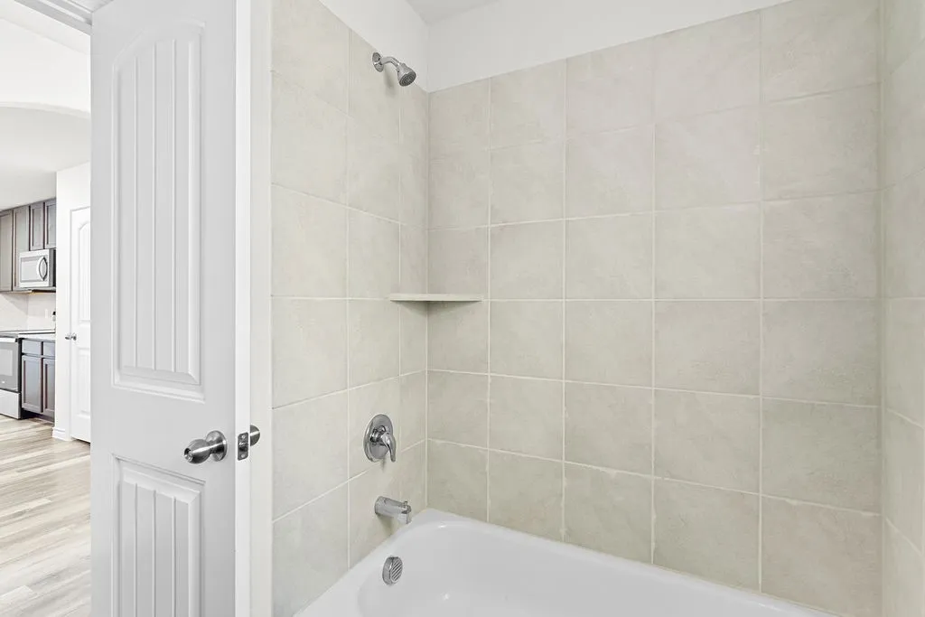 Bathtub and shower combination featuring neutral-toned tile surround, built-in shelf, and chrome fixtures