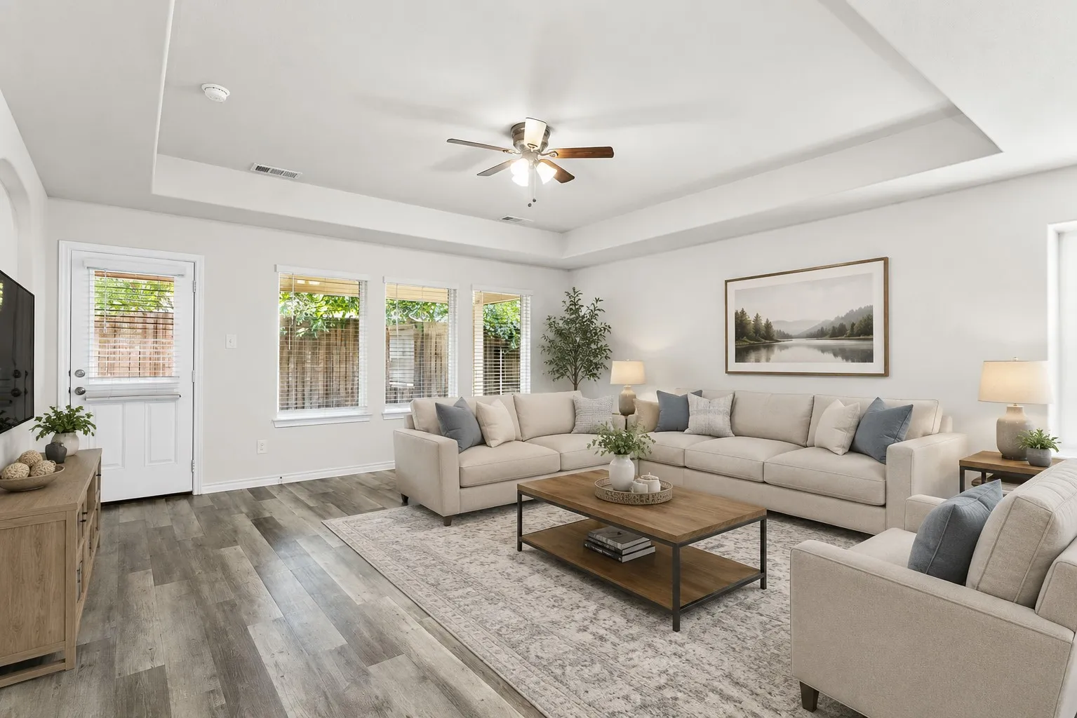Expansive living area featuring wood-finish flooring, a tray ceiling, ceiling fan, and multiple large windows
