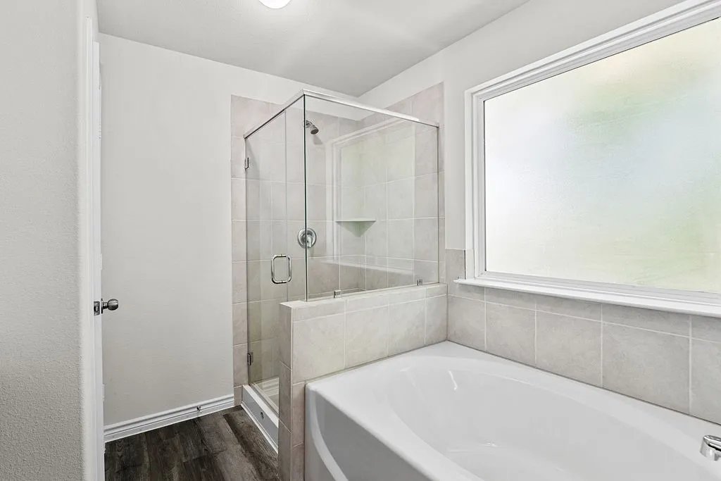 Freestanding soaking tub with tiled surround, glass-enclosed shower with tile, and wood-finish flooring