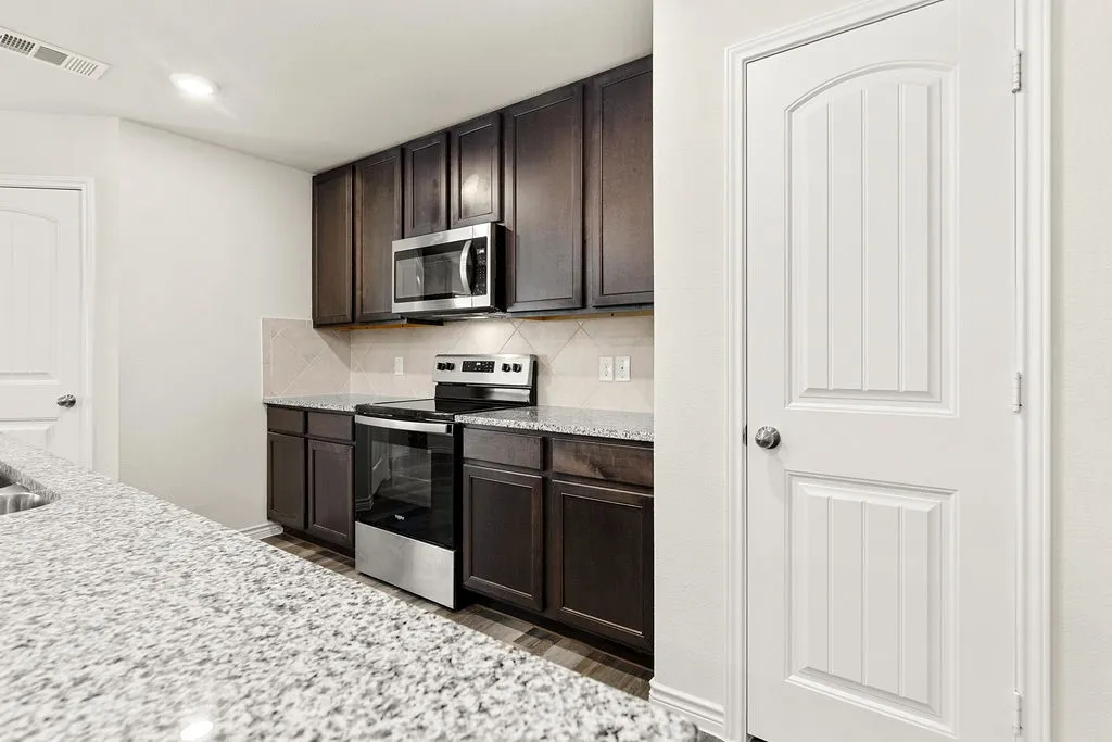 Kitchen featuring granite countertops, dark wood-finish cabinetry, stainless steel appliances, and a tiled backsplash