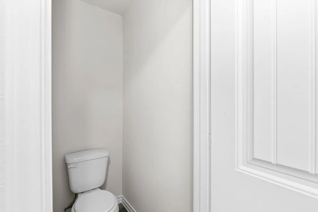 Recessed toilet alcove with light-toned walls and wood-finish flooring