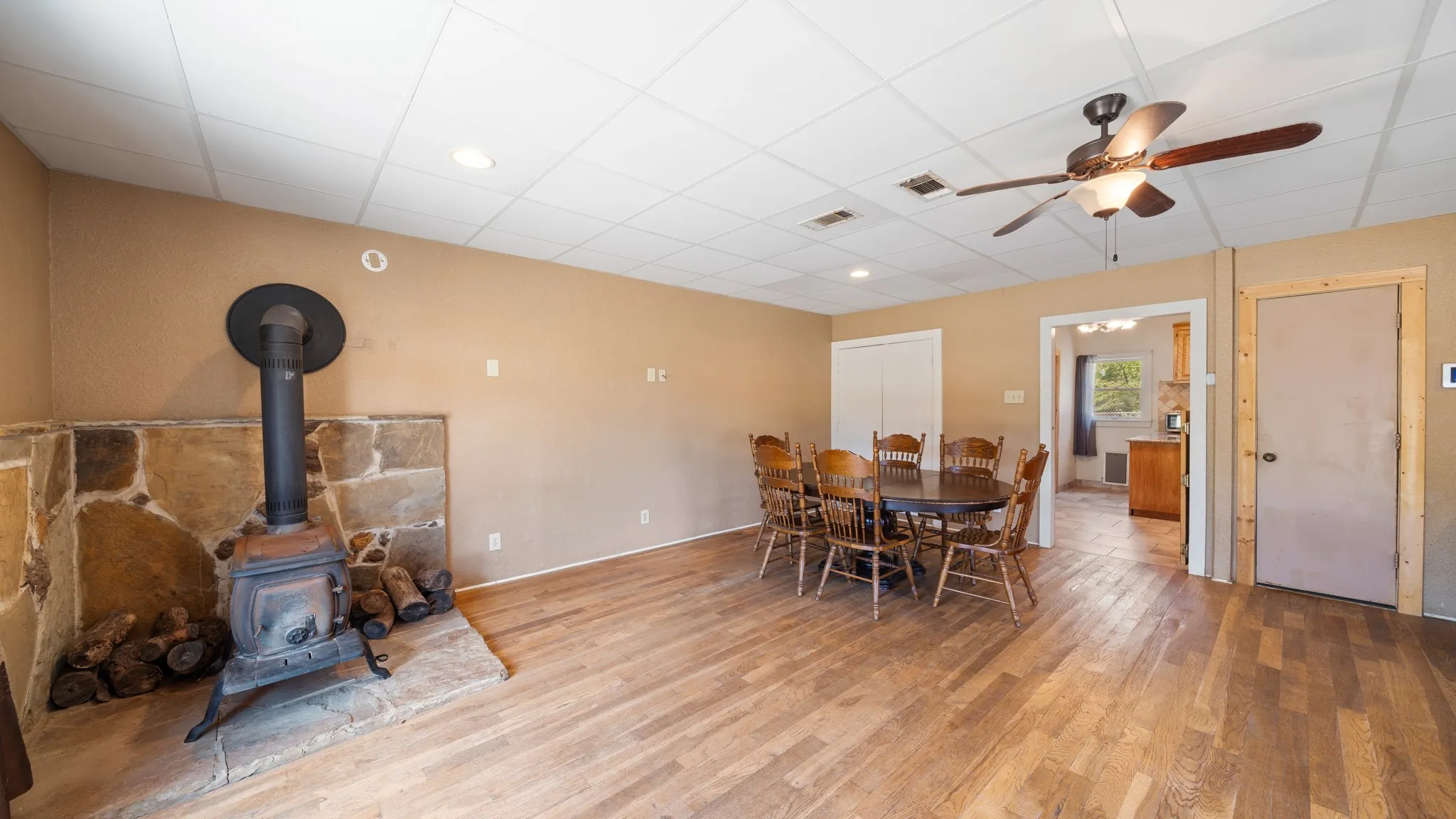 Wood-finish flooring throughout, stone-clad wood-burning stove, ceiling fan with integrated lighting, and recessed ceiling lighting