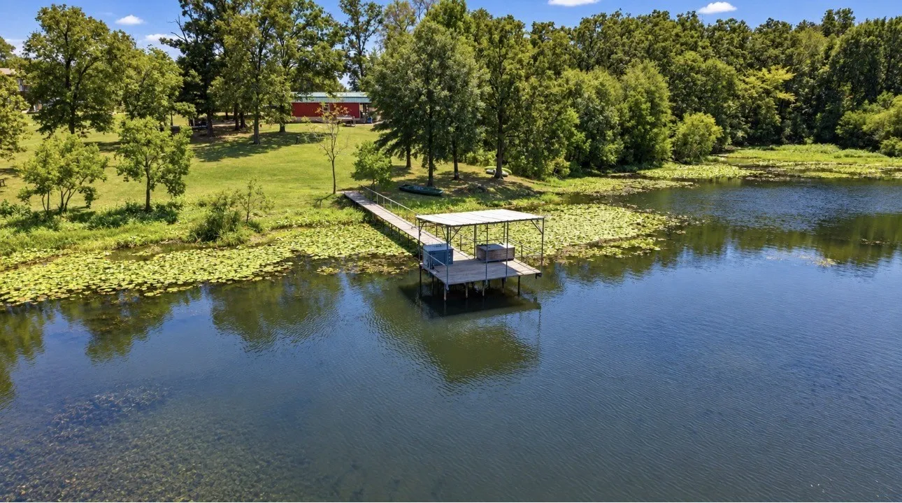 Waterfront property featuring a private dock with a covered boat slip, mature trees, and a spacious green lawn