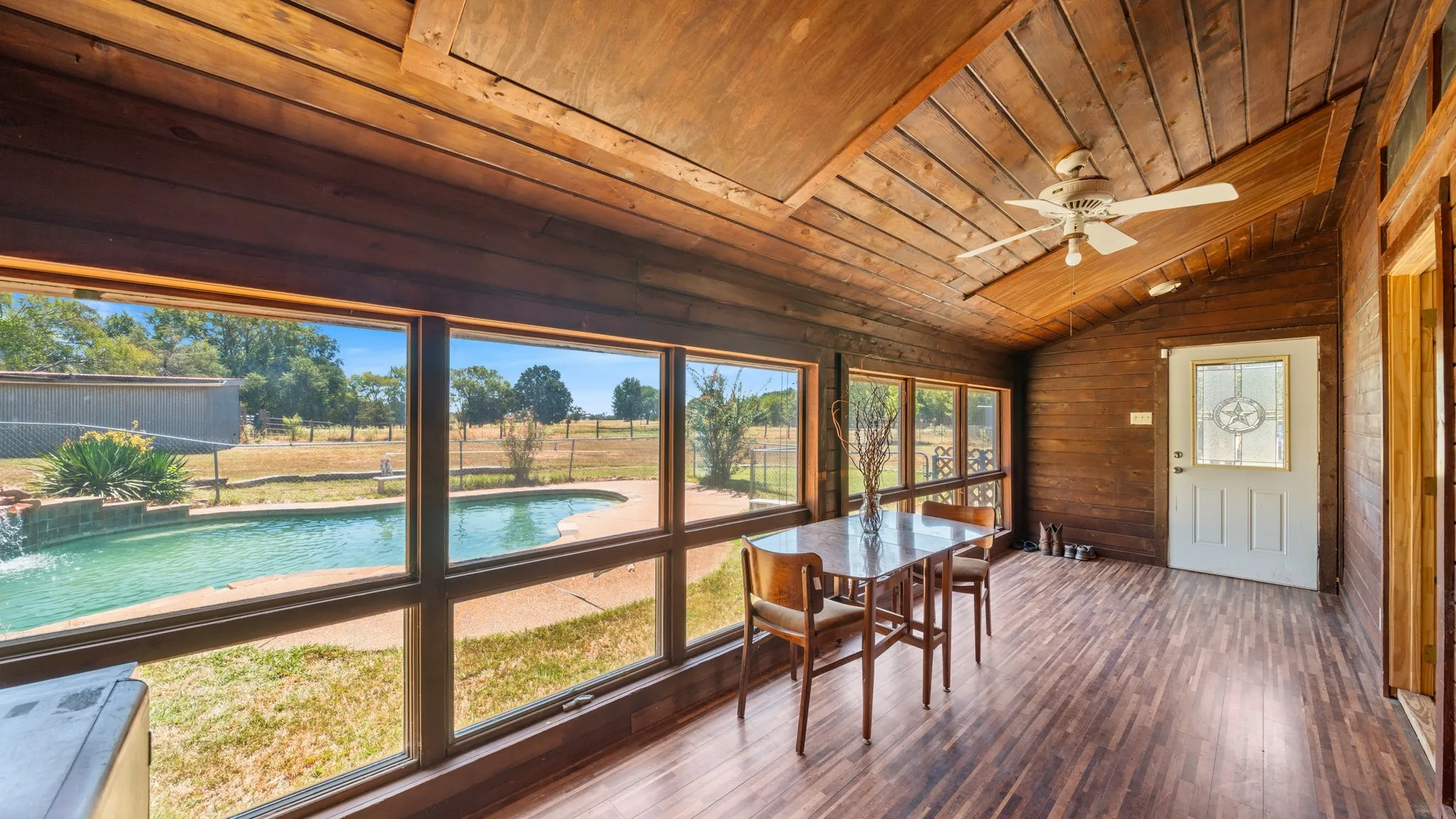 Wood-paneled sunroom with wood-finish flooring, vaulted ceiling, and an integrated ceiling fan