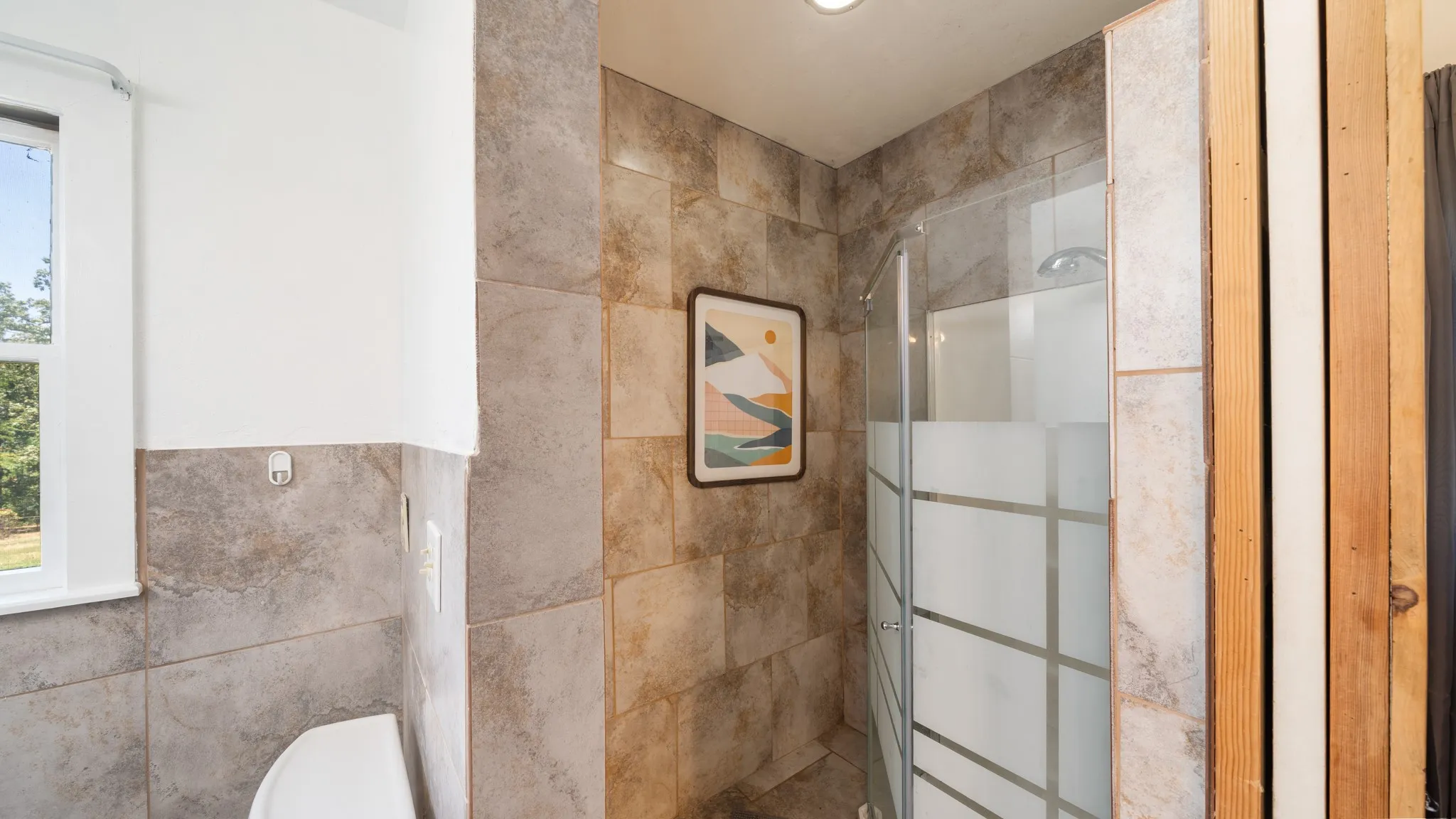 Tiled shower enclosure with a clear glass door, recessed lighting, and a white framed window