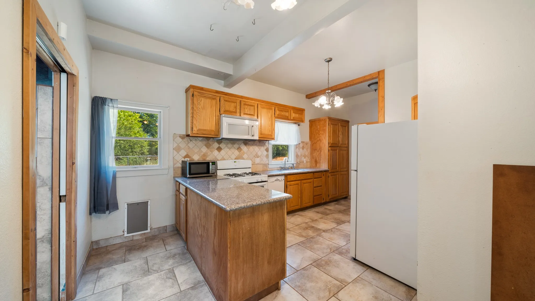 Kitchen featuring wood cabinetry, a center island with a granite-style countertop, a tile backsplash, and tile flooring