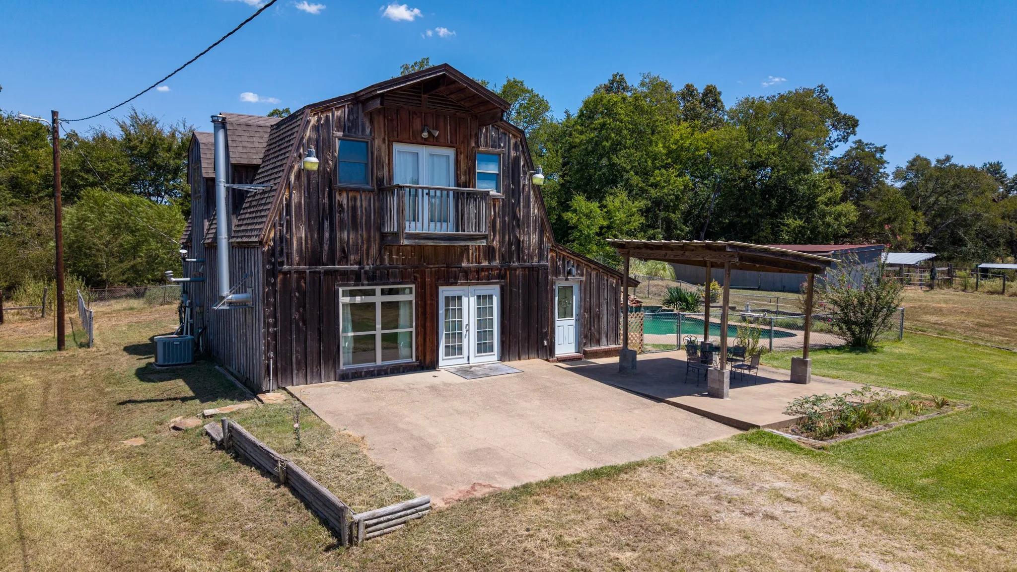 Two-story wood-sided structure with a balcony, an expansive concrete patio, a covered patio area, and a swimming pool
