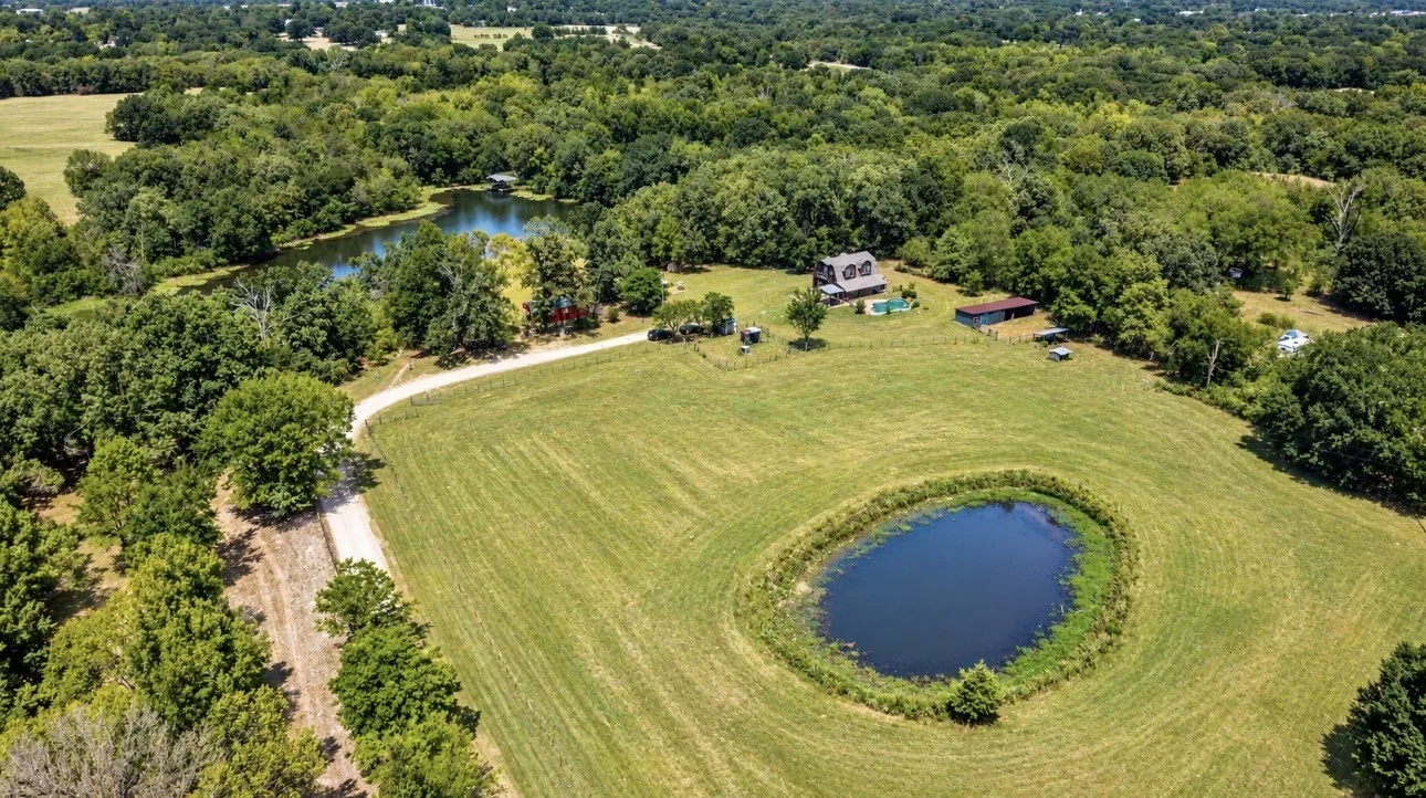 Expansive green landscape featuring two bodies of water, mature trees, and a winding dirt road