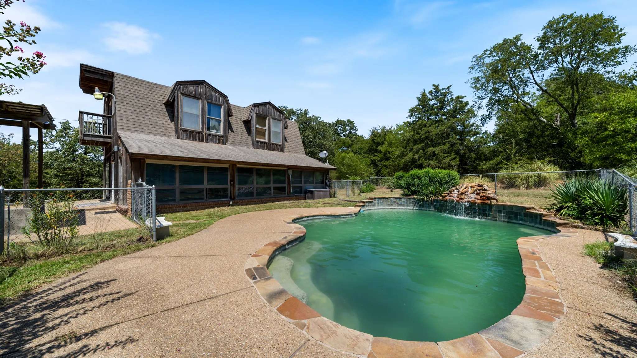 Freeform swimming pool with stone coping, an integrated waterfall feature, and surrounding concrete decking