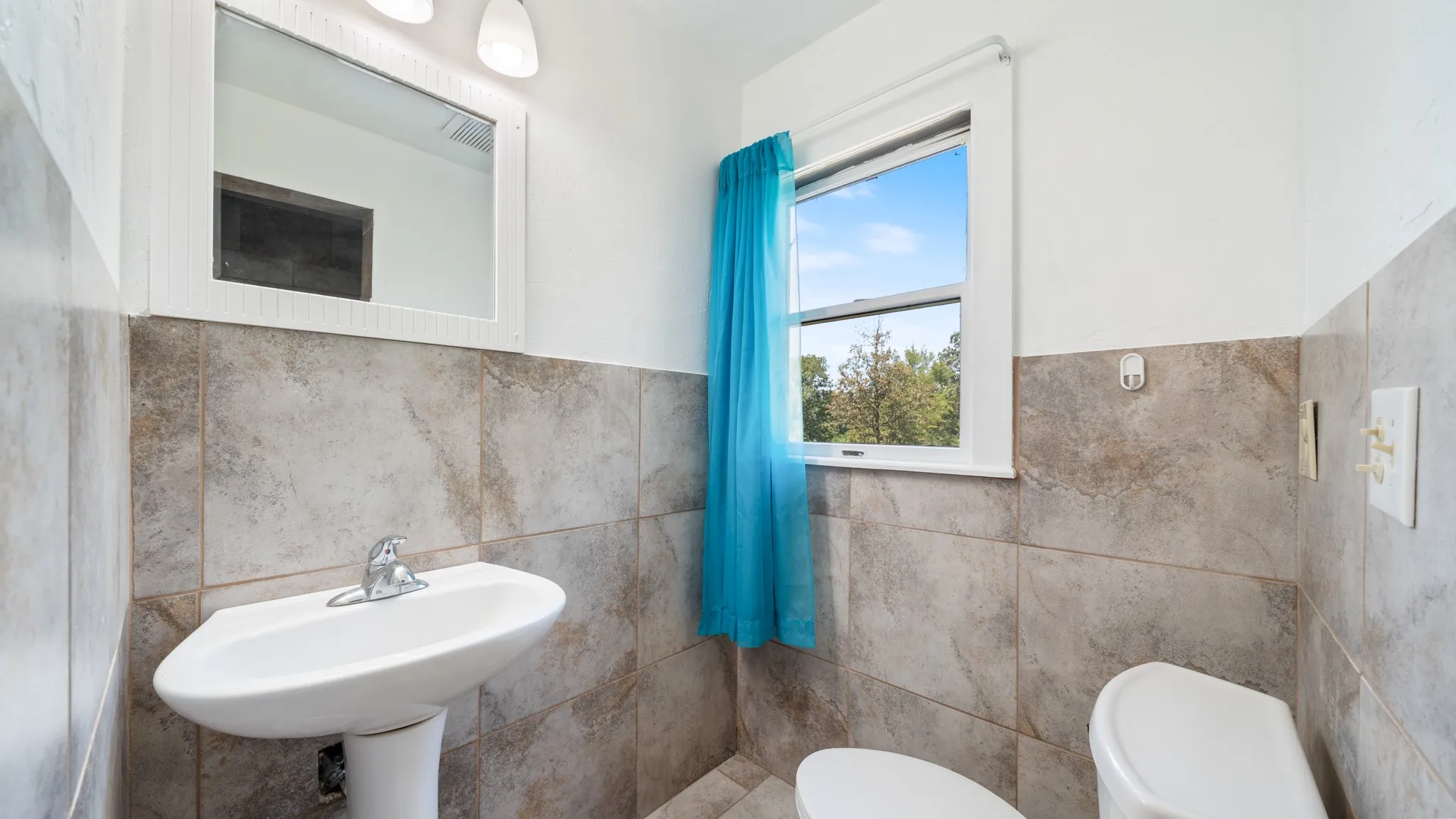 Pedestal sink with chrome faucet, framed mirror with vanity lighting, and wall-mounted toilet