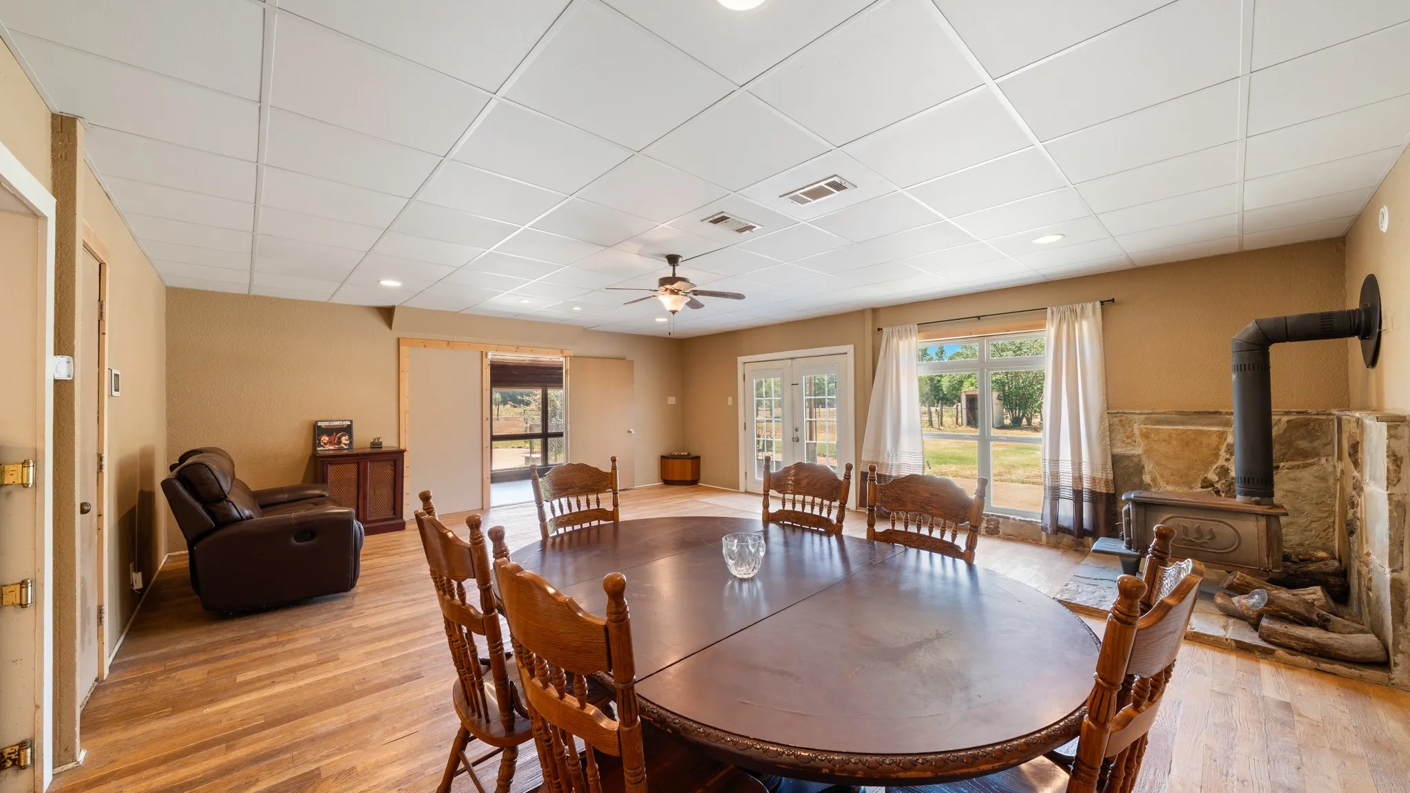 Spacious living area featuring wood-finish flooring, a stone-surround wood stove, and a ceiling fan