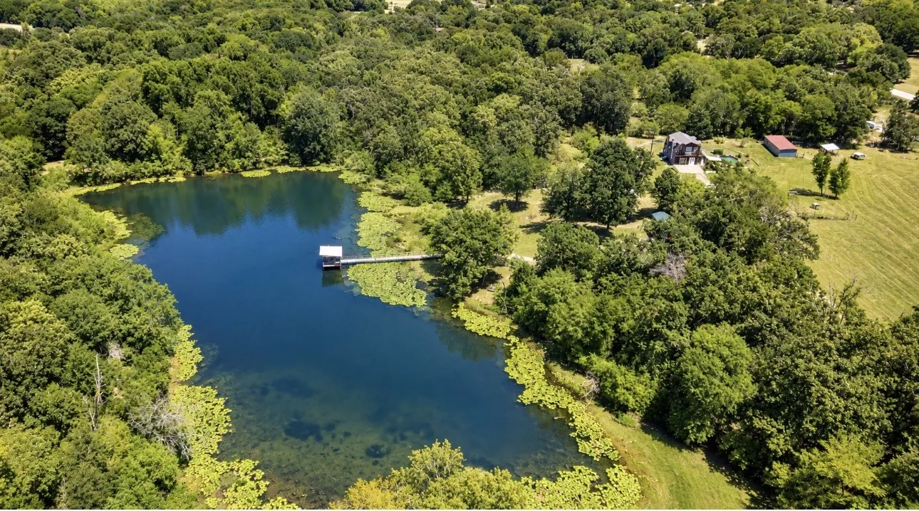 Expansive natural setting featuring a private pond with a dock, surrounded by mature trees and open fields