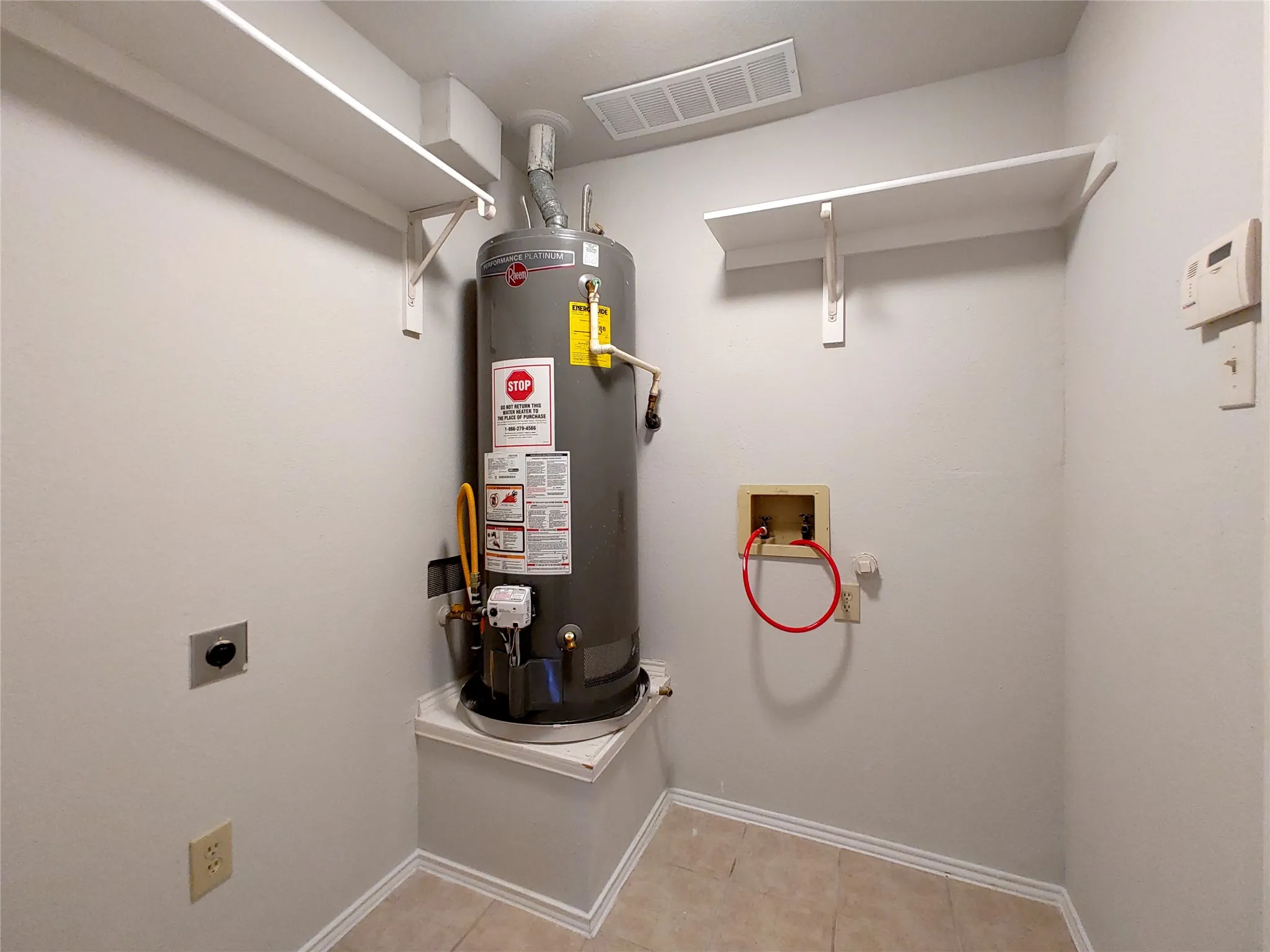 Utility area with wall-mounted shelving and tile flooring
