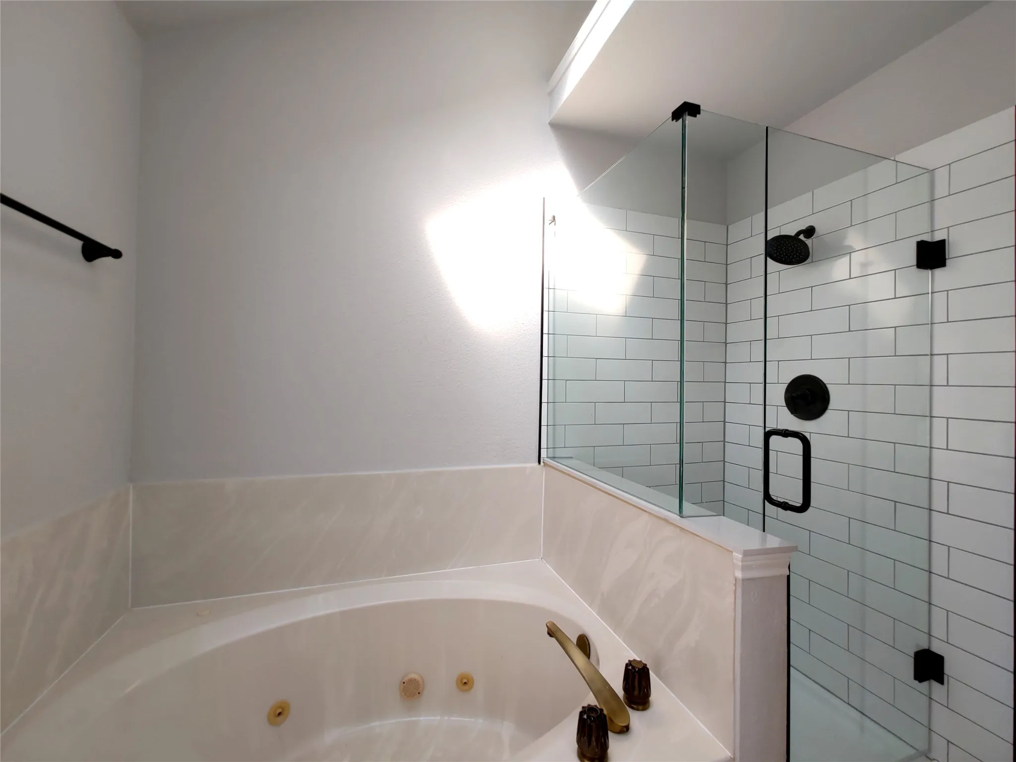 Jetted corner soaking tub with gold-tone fixtures, glass-enclosed shower with subway tile surround, and matte black shower fixtures