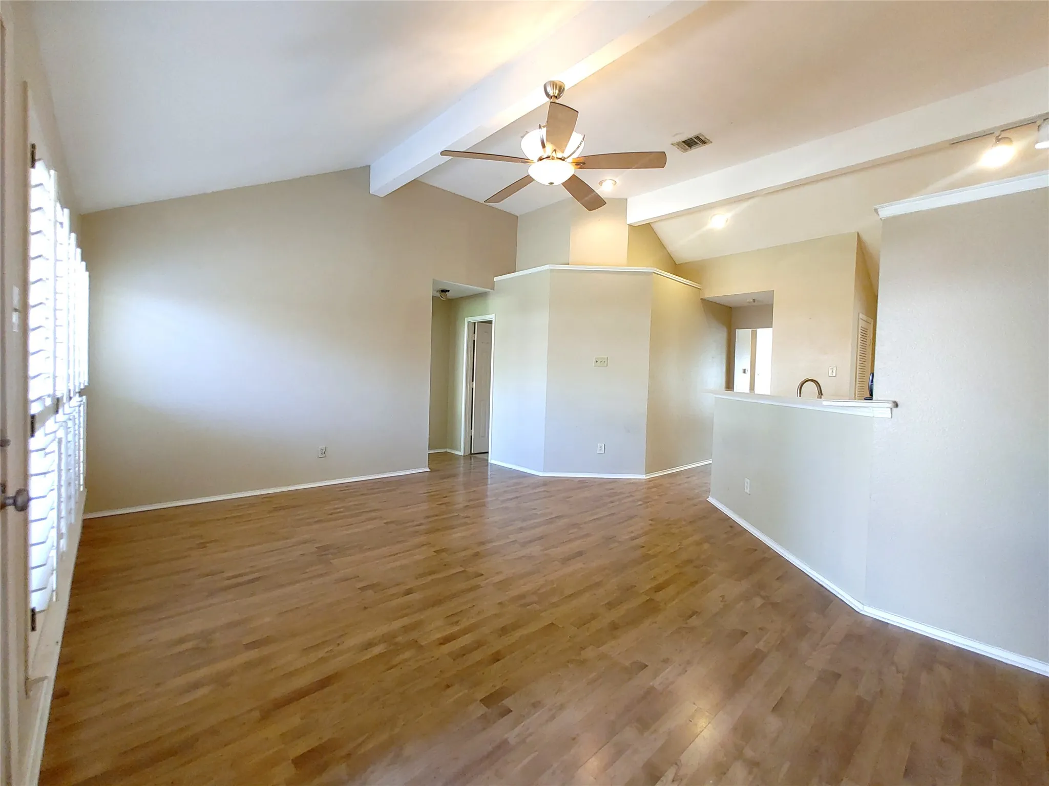 Vaulted ceiling with exposed beams, wood-finish flooring, ceiling fan, and track lighting