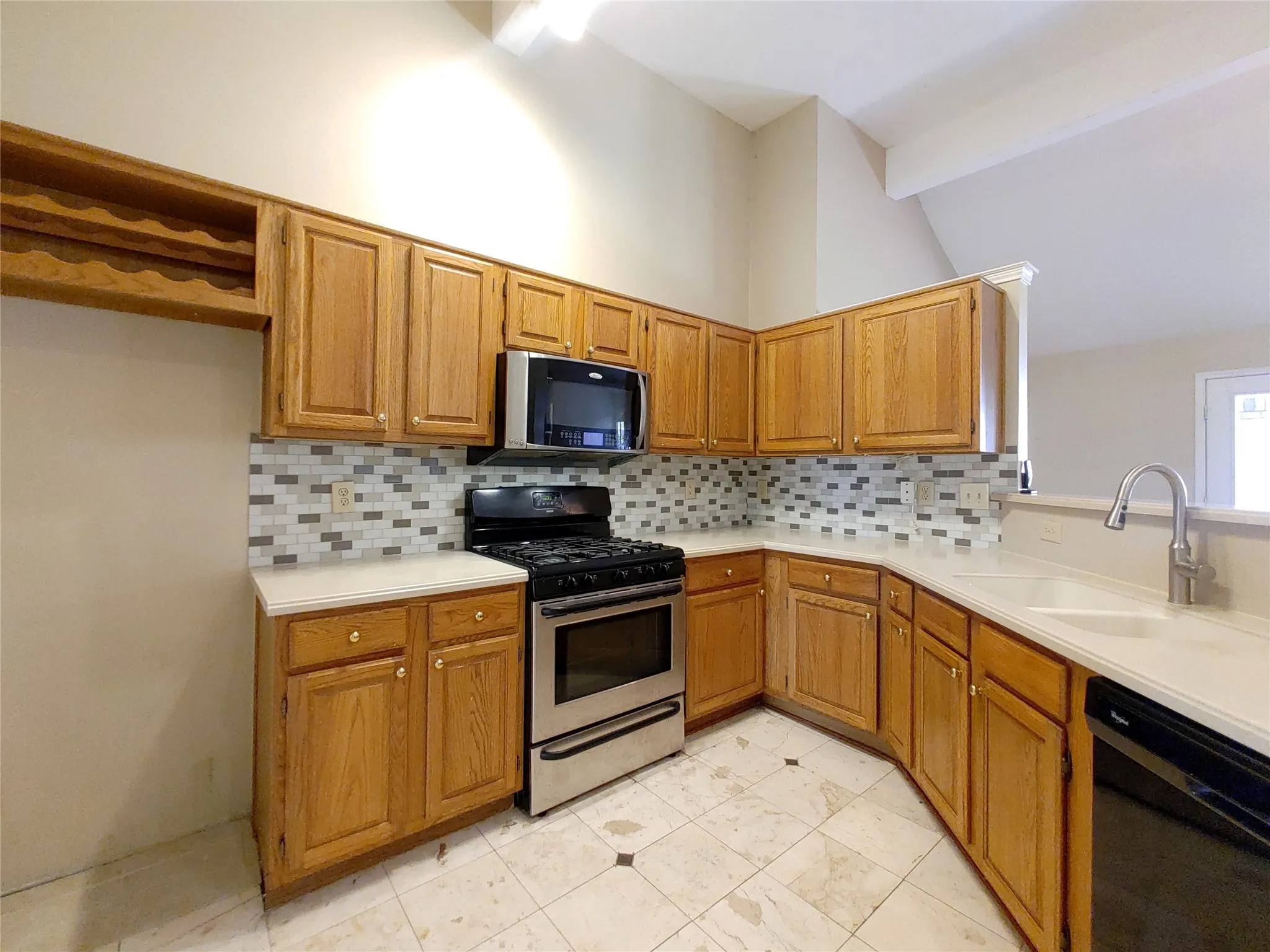 Kitchen featuring wood-finish cabinetry, stainless steel appliances, mosaic tile backsplash, a built-in wine rack, and a double basin sink