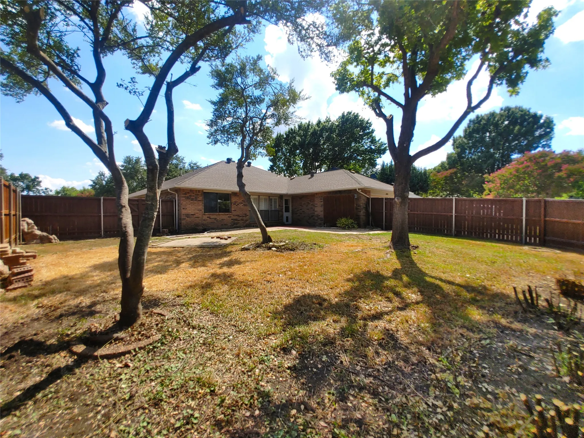 Brick exterior, asphalt shingle roof, mature trees, wooden privacy fence, concrete patio area