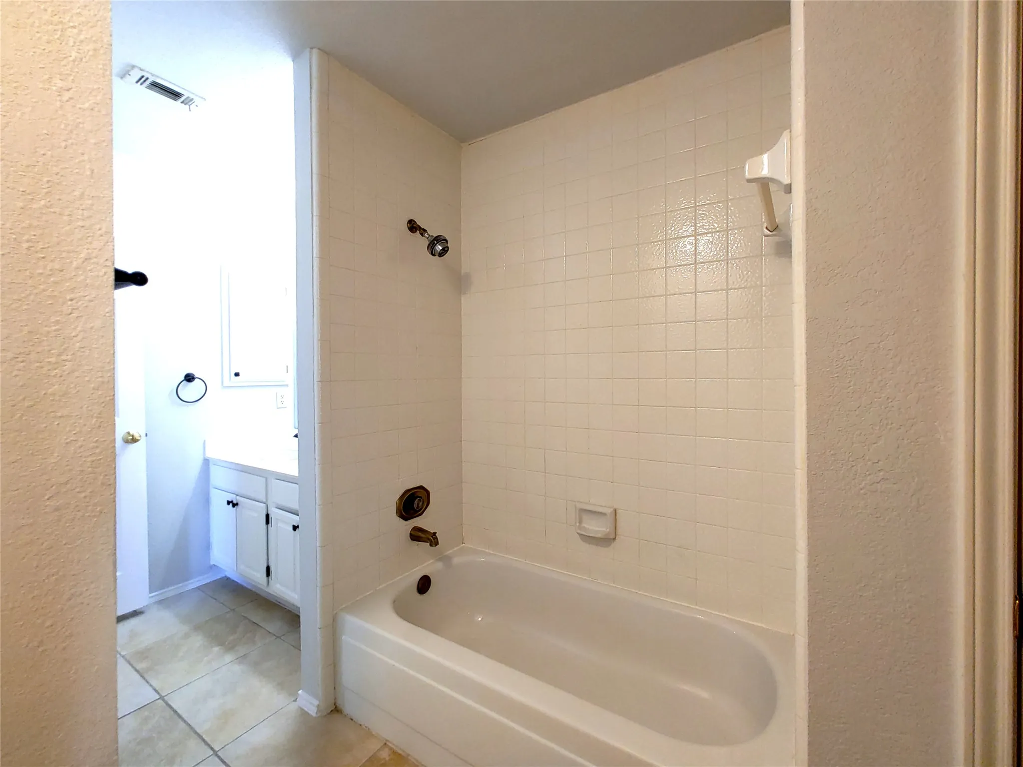 Bathtub with white tile surround, tub/shower combination, and wall-mounted showerhead