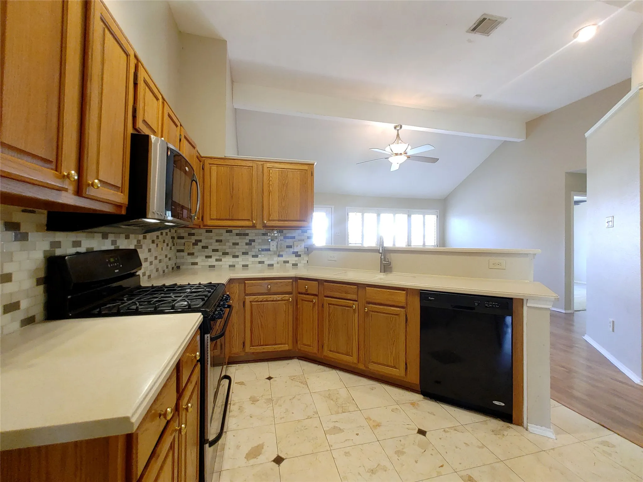 Kitchen featuring wood cabinetry, light-toned countertops, a mosaic tile backsplash, black appliances, and tile flooring