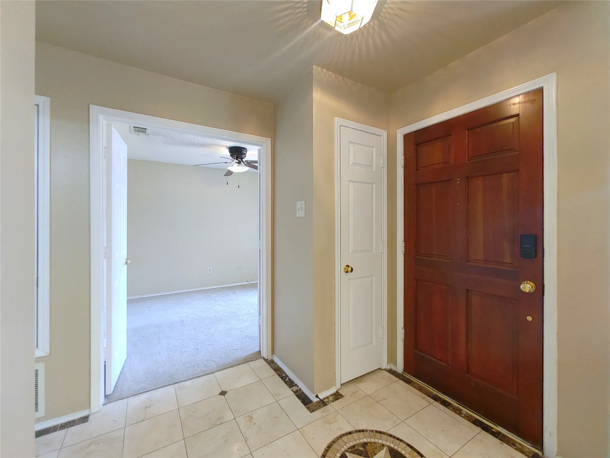 Hardwood entry door with brass hardware, tile flooring with a decorative inlay, recessed lighting, and an overhead ceiling fan in the adjacent room