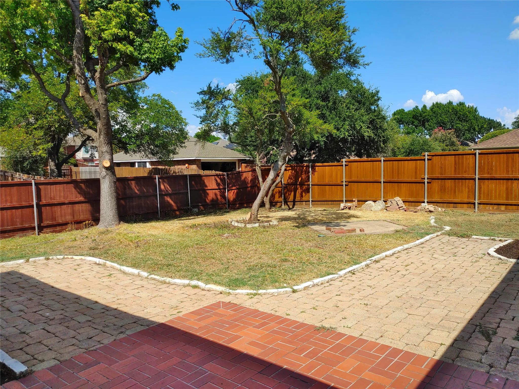 Private backyard featuring a wood privacy fence, mature trees, a red brick patio, and a paver pathway