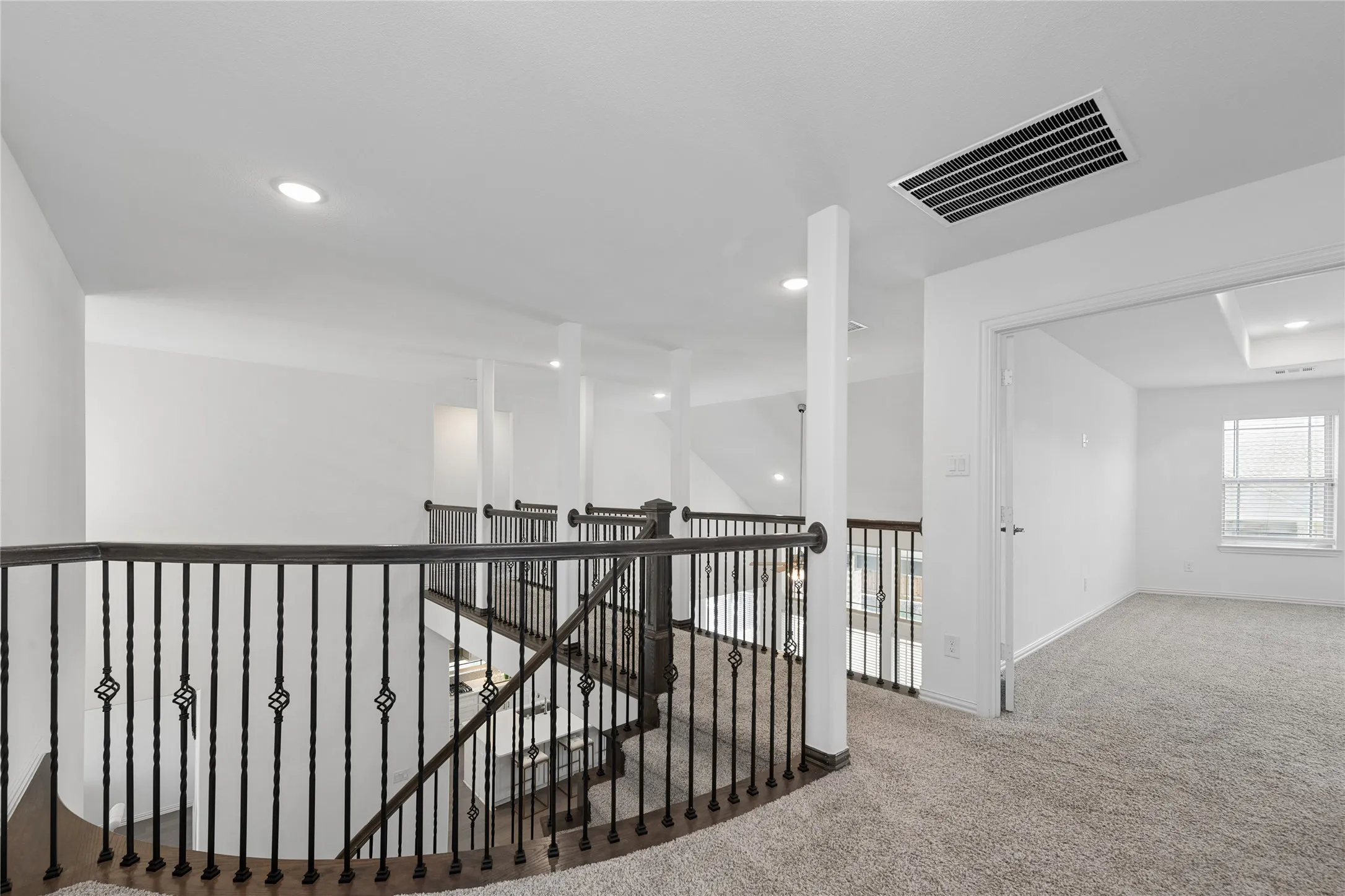 Upper level landing with wrought iron balusters, recessed lighting, carpet flooring, and a window for natural illumination