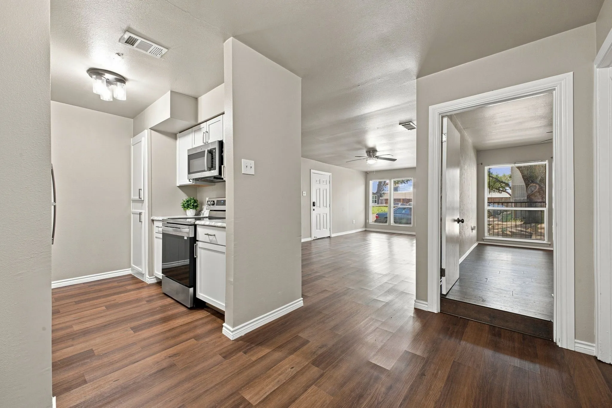 Wood-finish flooring throughout, white cabinetry with stainless steel appliances, and ceiling fans