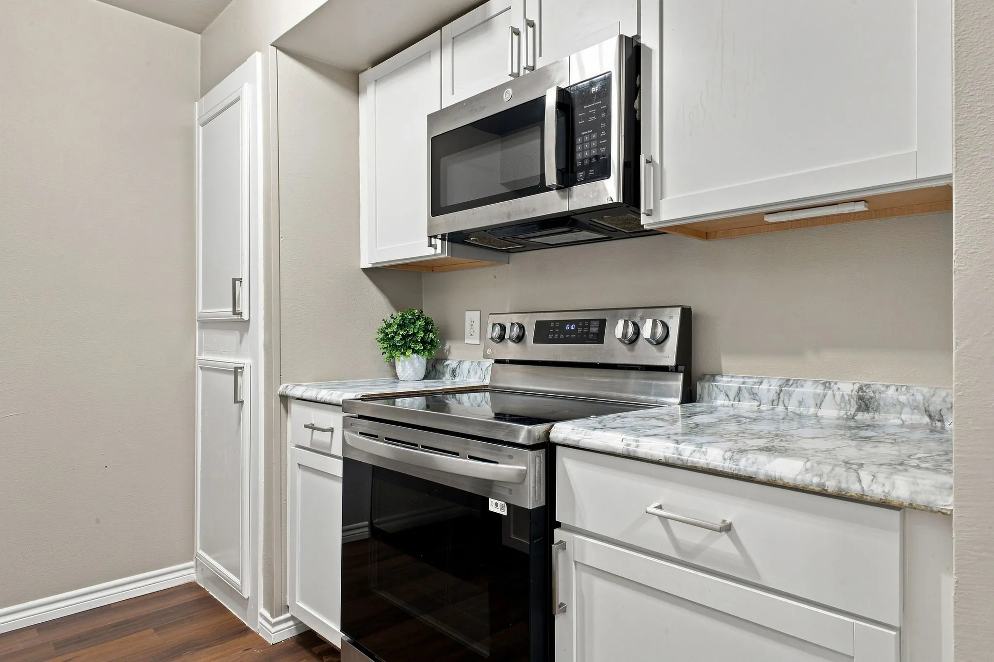 Stainless steel range, stainless steel microwave, white cabinetry, light-toned countertops with dark veining, and wood-finish flooring