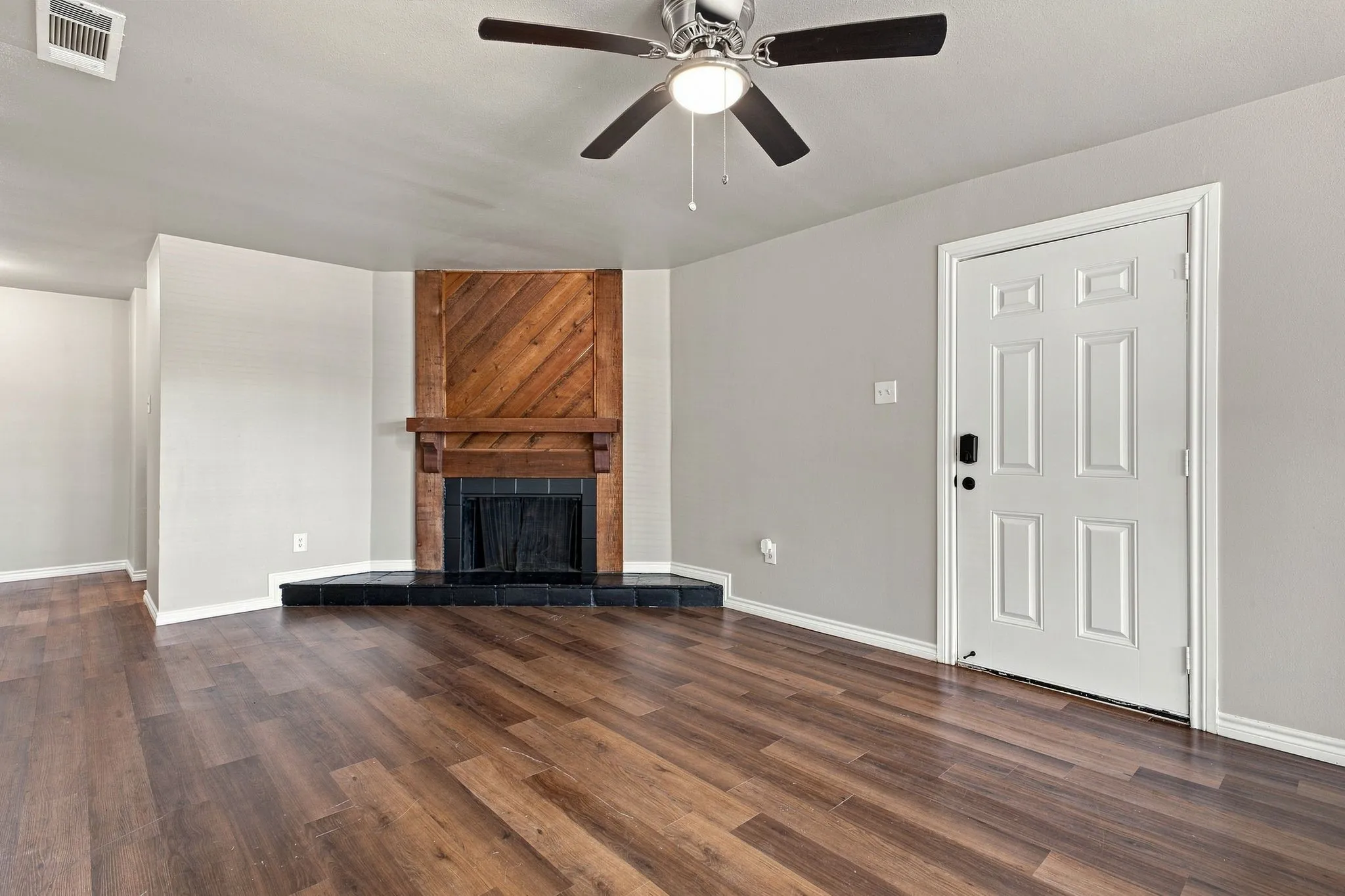 Wood-finish flooring throughout, featuring a corner fireplace with a black tile hearth and a wood-paneled accent wall