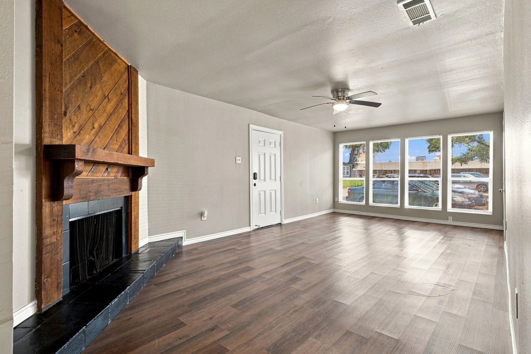 Hardwood-finish flooring, wood-paneled fireplace with a dark tile hearth, ceiling fan with integrated lighting, and multiple large windows