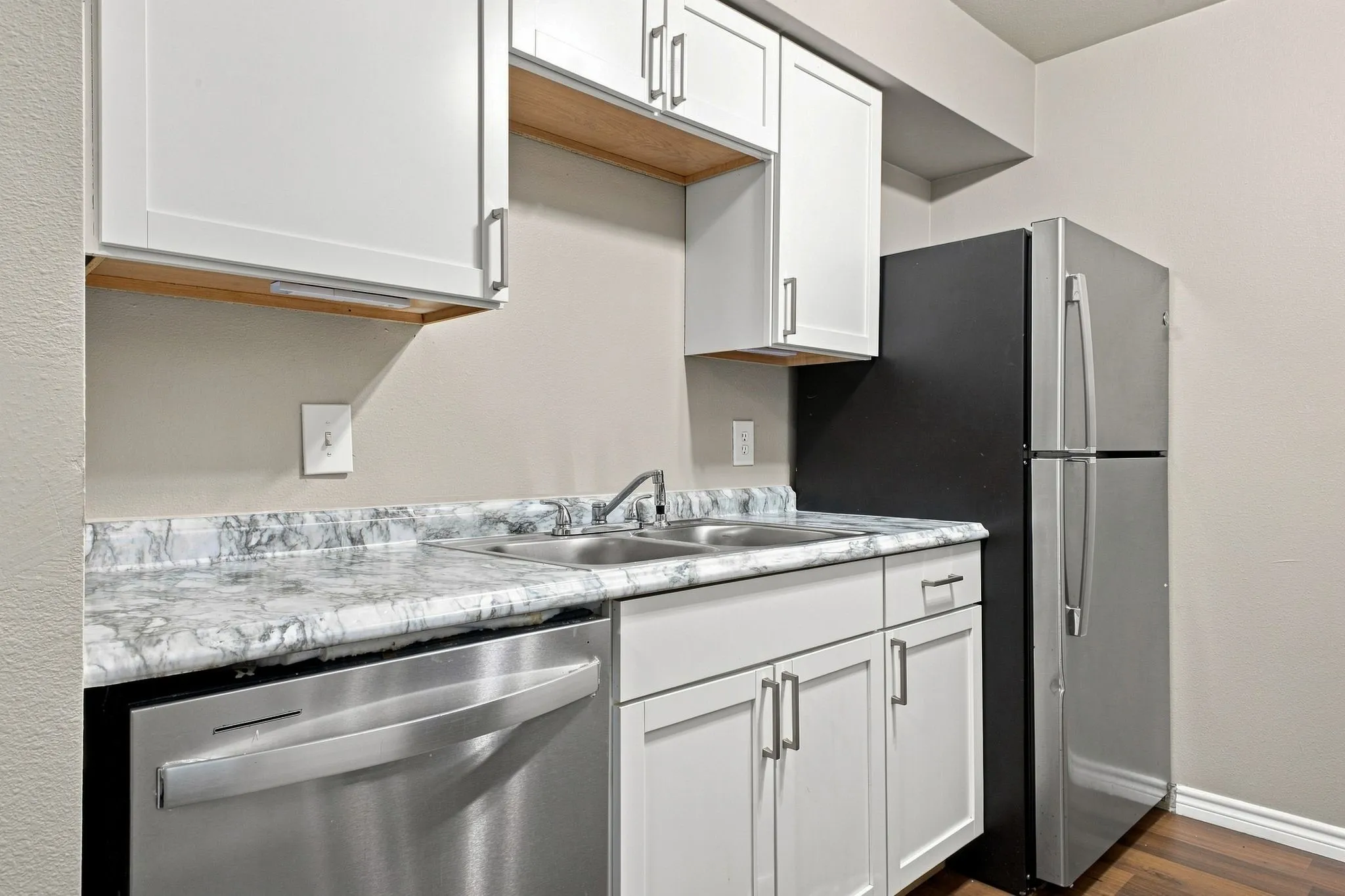 White cabinetry with brushed nickel hardware, stainless steel sink, wood-finish flooring, and a stainless steel dishwasher