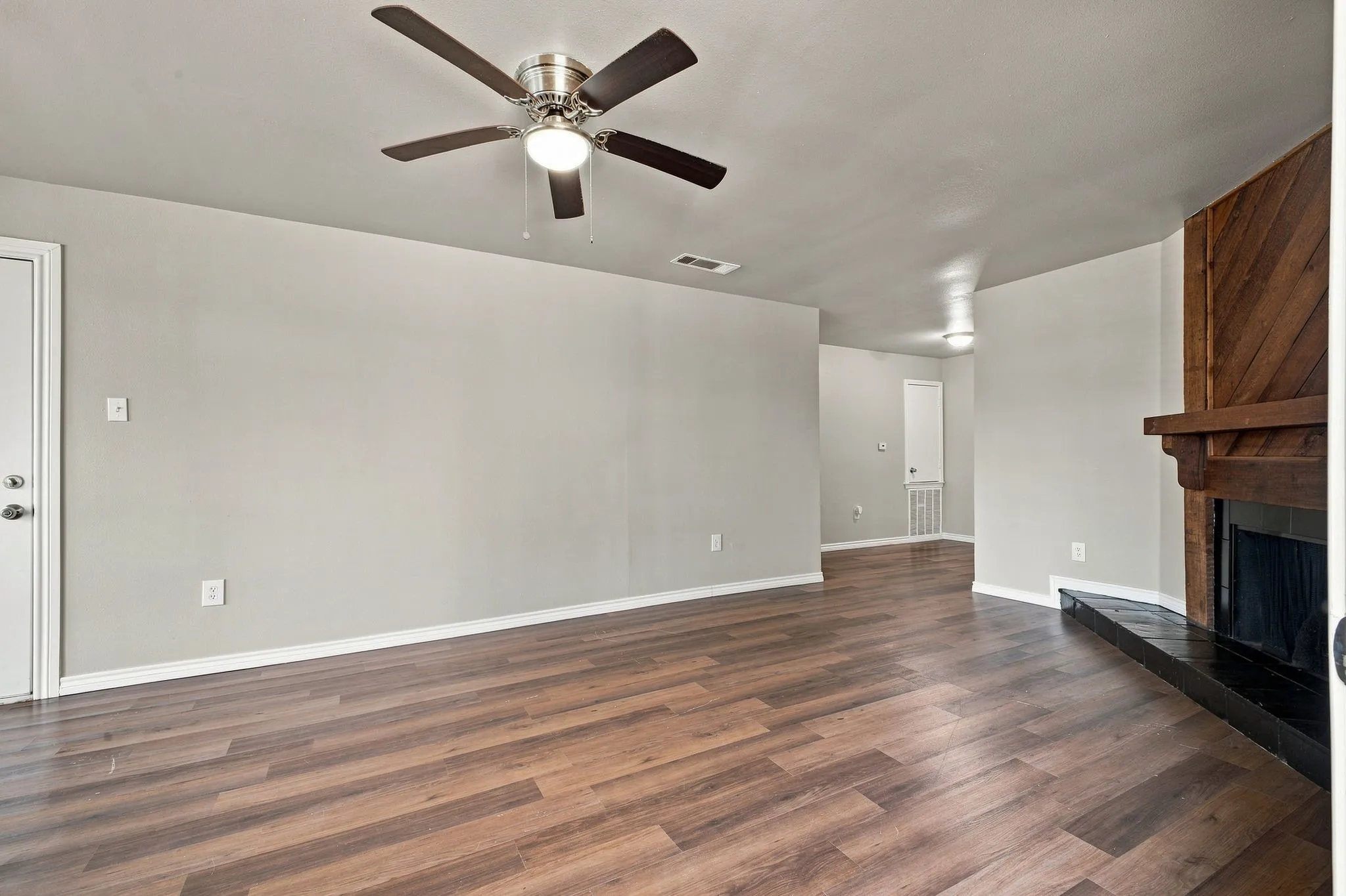 Spacious room featuring wood-finish flooring, a ceiling fan with integrated lighting, and a fireplace with a wood mantel and black hearth
