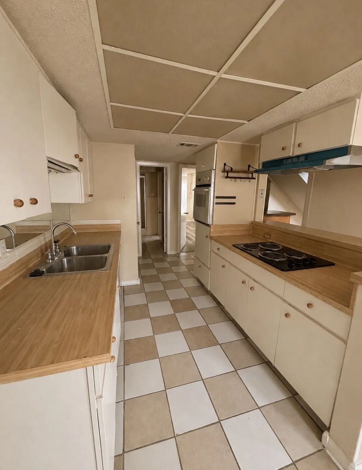 Galley-style kitchen with dual basin stainless steel sink and checkerboard tile flooring, built-in oven, and electric cooktop
