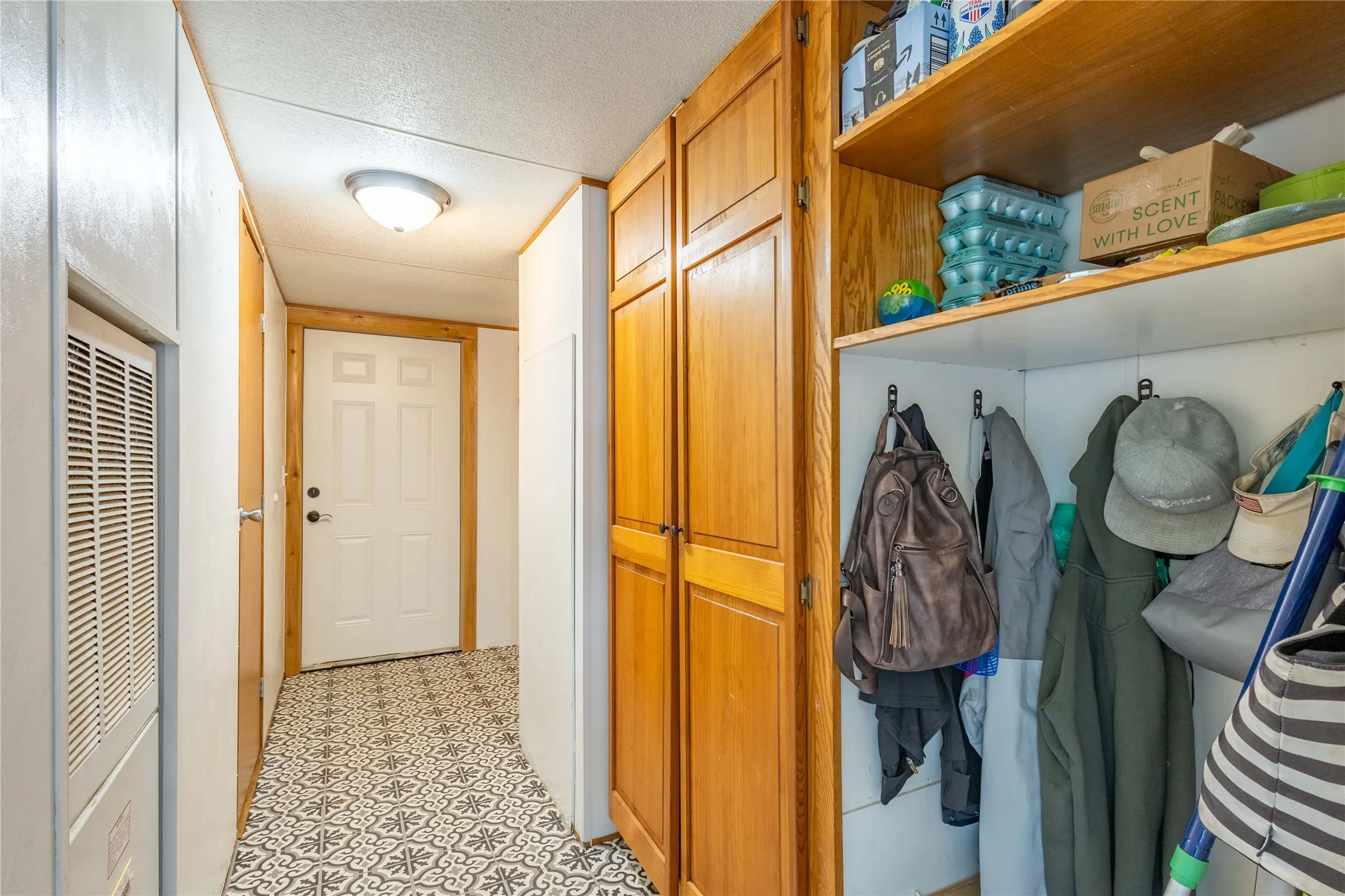 Patterned floor tiles and flush-mount ceiling lighting illuminate a hallway featuring a built-in wooden storage cabinet with shelving and coat hooks