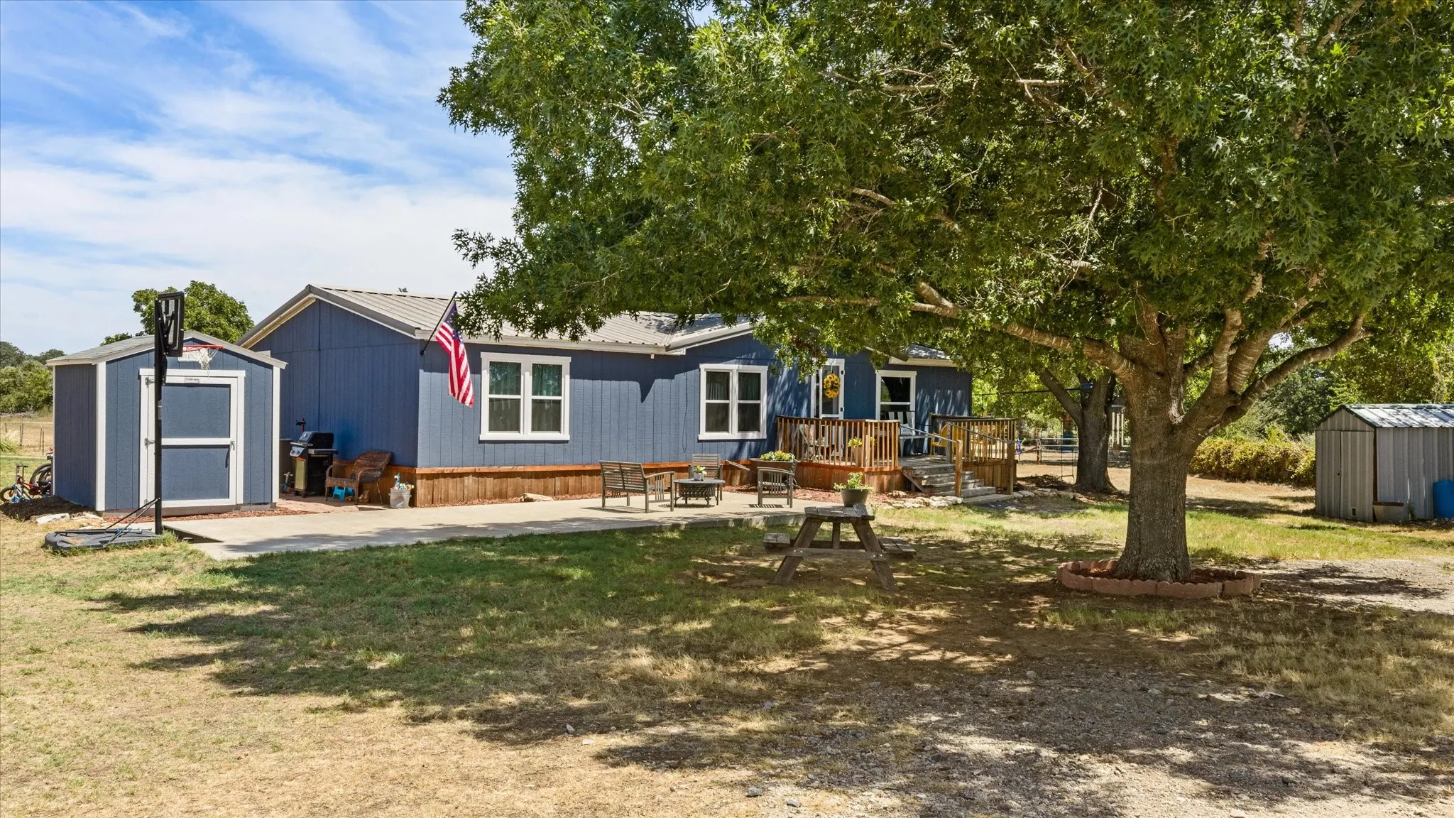 Blue exterior siding with white trim, new windows, a metal roof, a wood deck and concrete patio for entertaining