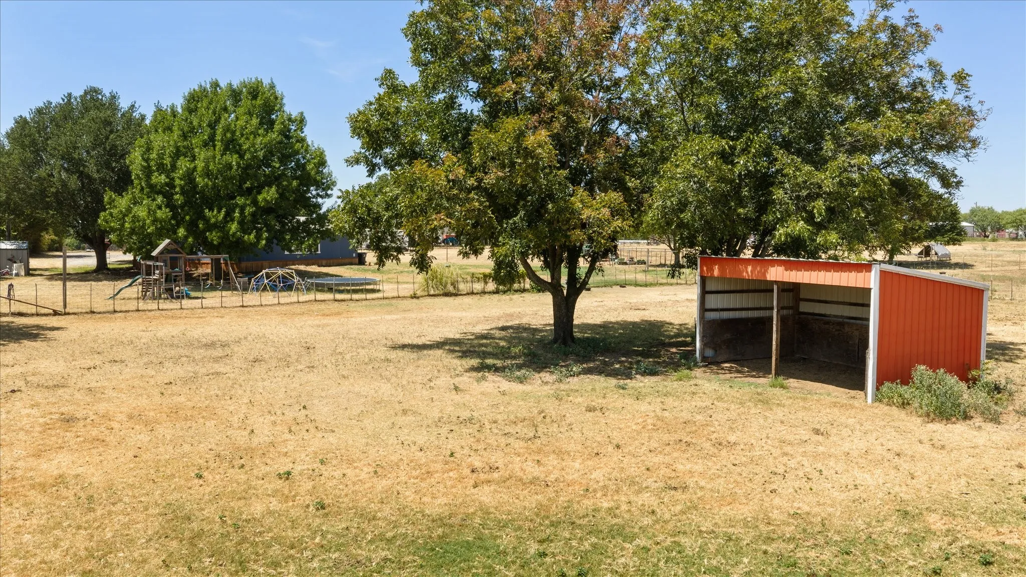 Expansive horse pen featuring an open-sided metal 12x20 horse shed with a red exterior