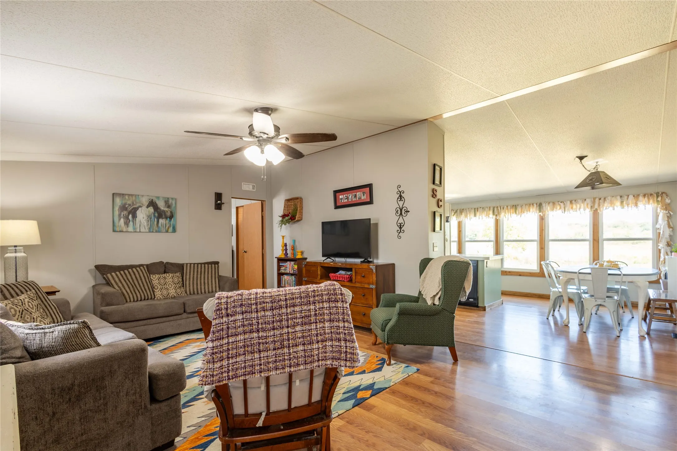 Spacious common area featuring wood-finish flooring, a ceiling fan with integrated lighting, and multiple windows