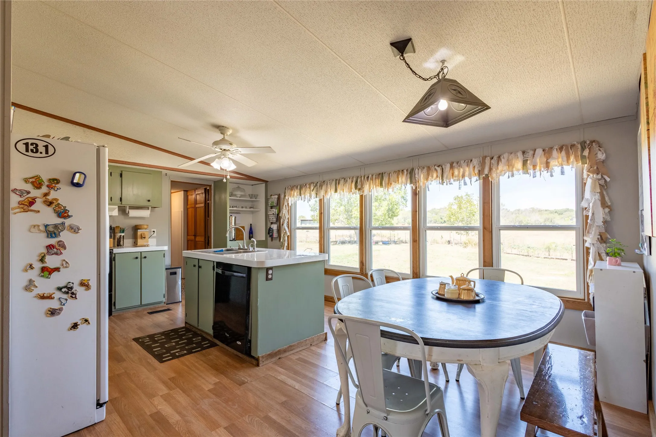 Kitchen featuring a ceiling fan, recessed lighting, wood-finish flooring, a central island with an integrated sink, and multiple windows