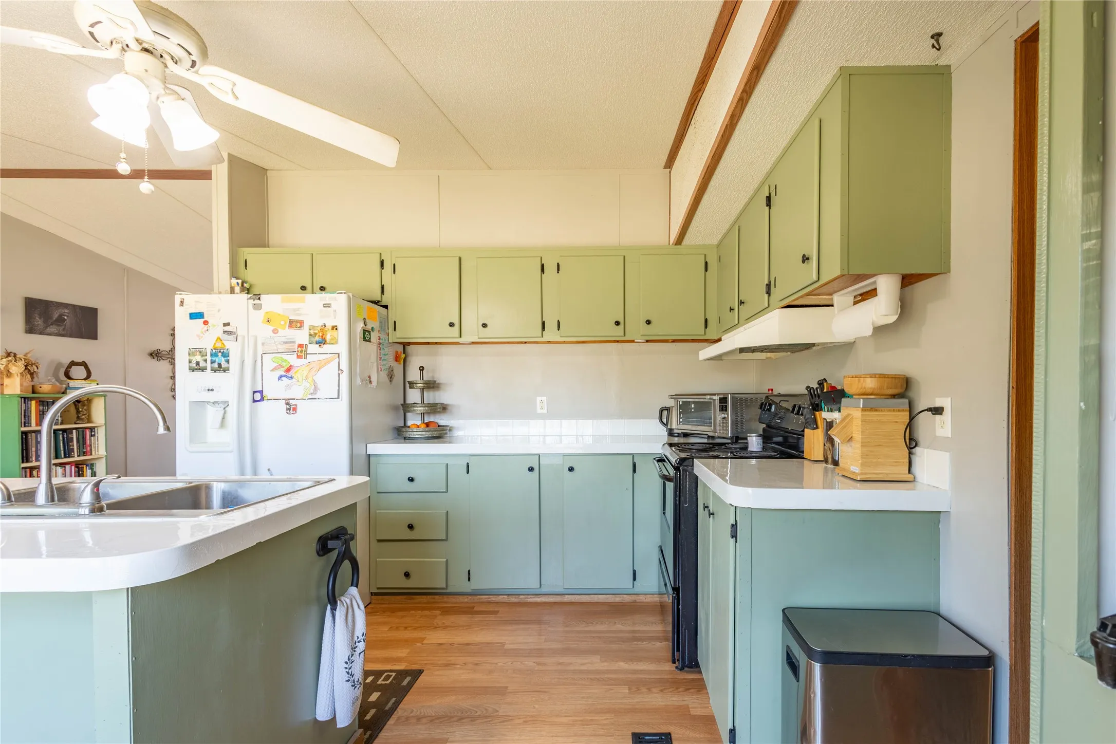 Kitchen featuring light green cabinetry, white countertops, wood-finish flooring, and a ceiling fan